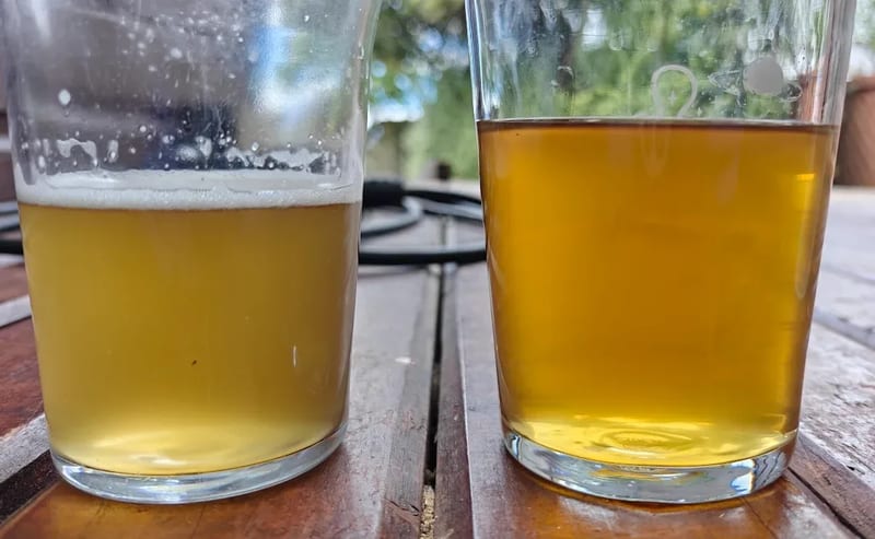 Two glasses side by side on an outdoor table: the pale, hazy reserve beer on the left and the deeper gold, bright barrel sample on the right