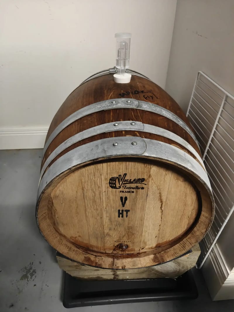 The 57 L Villard Tonnellerie barrel lying on a timber cradle in a corner, airlock in the bung